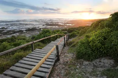 a wooden stairs leading down to the ocean at sunset at Anchor's Rest in Hermanus