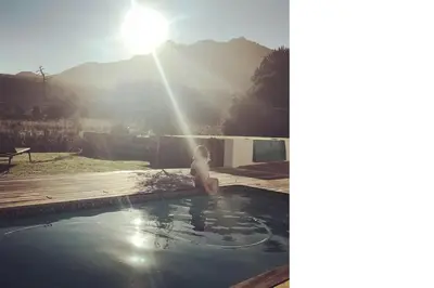 a boy sitting in a swimming pool with the sun shining at Charming Villa in Stellenbosch
