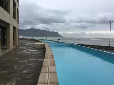 a blue swimming pool next to the ocean at Ocean View Luxury Self-Catering in Strand