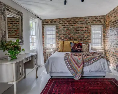 a bedroom with a bed and a brick wall at De Kale Kat in Greyton