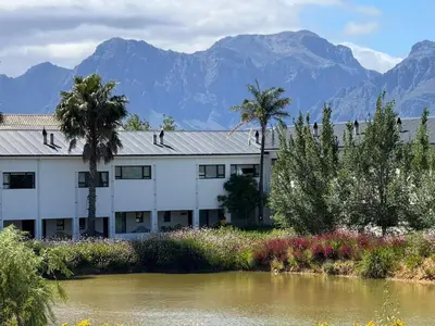 a building next to a river with mountains in the background at Middelplaas Paarl Guesthouse in Paarl