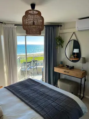 a bedroom with a bed and a desk with a view of the ocean at Abode Africa in Bloubergstrand
