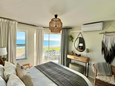 a bedroom with a bed and a desk with a view of the ocean at Abode Africa in Bloubergstrand