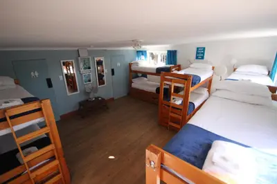 a room with four bunk beds and a room with wooden floors at Saltycrax Backpackers and Surf Hostel in Bloubergstrand