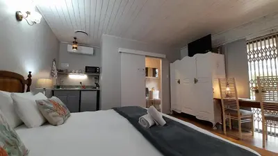 a bedroom with a large white bed and a kitchen at Vergenoegd Guesthouse in Panorama