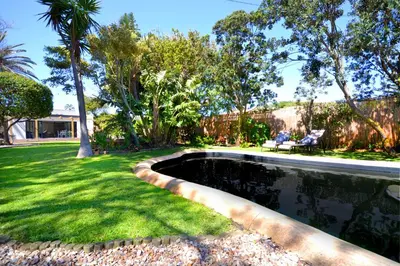 a swimming pool in a yard with grass and trees at SAFFRON COTTAGE in Hermanus