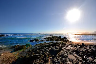 a beach with rocks and the sun in the sky at SAFFRON COTTAGE in Hermanus