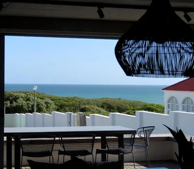 a table and chairs on a balcony with the ocean at Troon Beach Cottage Hermanus in Hermanus