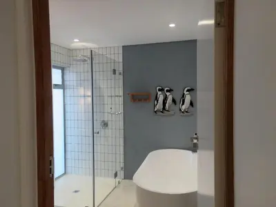 a bathroom with a shower with penguins on the wall at Troon Beach Cottage Hermanus in Hermanus