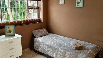a bedroom with a bed and a dresser and two windows at Blouberg Beach Retreat in Bloubergstrand