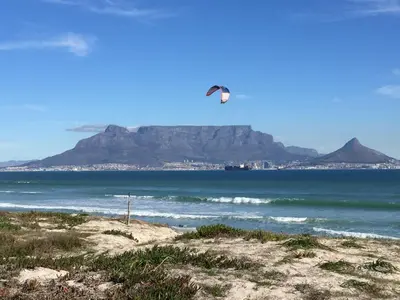 a kite flying over the ocean with a mountain in the background at Portico 606 in Bloubergstrand