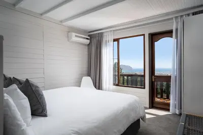 a bedroom with a white bed and a large window at Lalapanzi Lodge in Somerset West