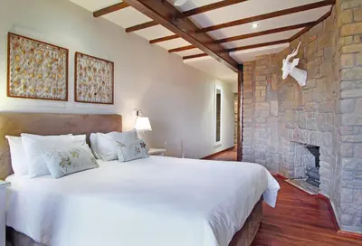 a bedroom with a large bed and a stone fireplace at Lalapanzi Lodge in Somerset West
