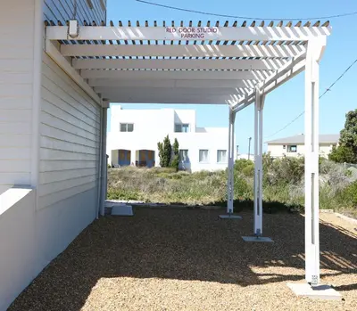 a white pergola with a building in the background at Reddoor Studio in Pringle Bay
