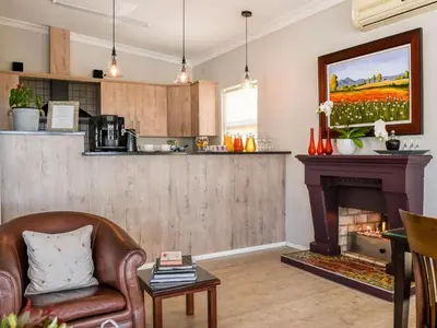 a living room with a fireplace and a kitchen at Four Palms Accommodation in Durbanville