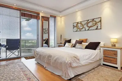 a bedroom with a large bed and a balcony at Dolphin Beach E5 in Bloubergstrand