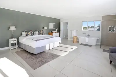 a bedroom with a large bed and a tub and a sink at 269 on Main Holiday Home in Hermanus