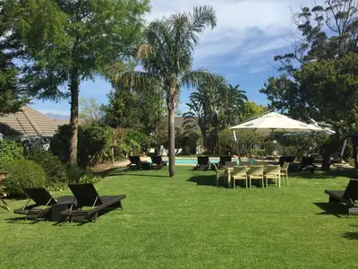 a lawn with chairs and an umbrella and a pool at Albourne Guesthouse in Somerset West