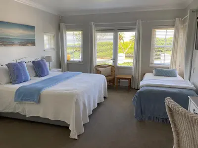 a bedroom with two beds with blue pillows and windows at Shore's Edge Luxury Oceanfront Home in Hermanus