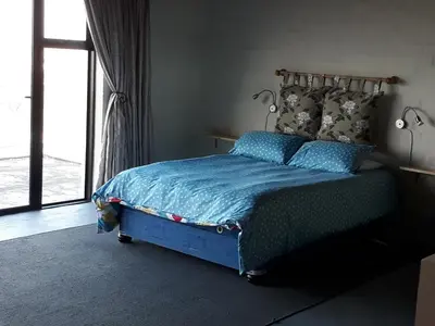 a bedroom with a bed with a blue comforter and a window at Jack's Seaview in Bettyʼs Bay