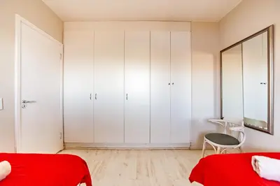 a bedroom with white cabinets and a red bed at Luxury Private Beachfront 2 bedroom Dolphin Apartment, Blouberg, Cape Town in Bloubergstrand