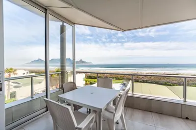 a dining room with a table and chairs and the ocean at Luxury Private Beachfront 2 bedroom Dolphin Apartment, Blouberg, Cape Town in Bloubergstrand