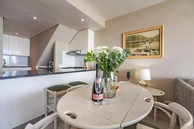 a dining room table with a vase of flowers on it at Luxury Private Beachfront 2 bedroom Dolphin Apartment, Blouberg, Cape Town in Bloubergstrand