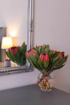 a vase of flowers on a table in front of a mirror at Brookshill - Protea suite in Somerset West