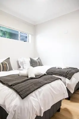 a bedroom with two beds with white walls and a window at Skinkikofi Guest House in Paarl