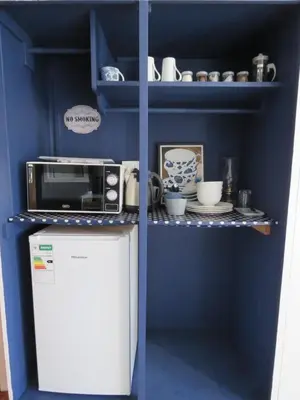 a blue kitchen with a microwave and a refrigerator at Koraalboom Guesthouse in Wolseley