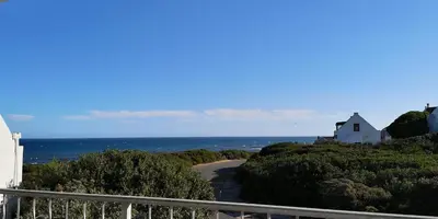 a white house on a hill next to the ocean at Beach Cottage 2 in Hermanus