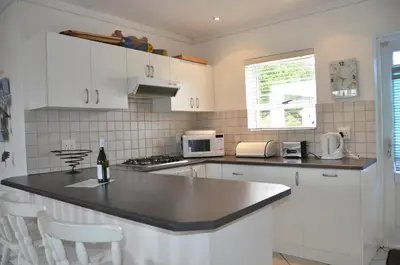 a kitchen with white cabinets and a black counter top at Beach Cottage 2 in Hermanus