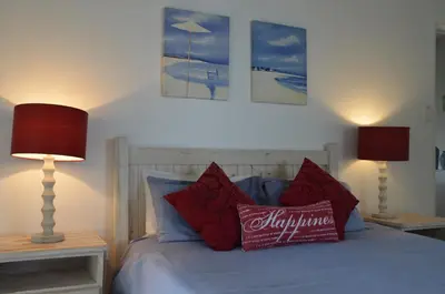 a bedroom with a bed with red pillows and two lamps at Beach Cottage 2 in Hermanus