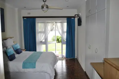 a bedroom with a bed with blue curtains and a window at Cotswold House Residence in Cape Town