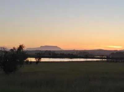 a sunset over a field with a body of water at Wild Clover Cottages in Stellenbosch