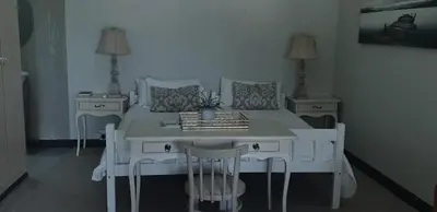a bedroom with a white bed with two tables and chairs at Ladera - Vista Self-catering Guesthouse in Paarl