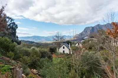 a white house on a hill with mountains in the background at Bartinney Private Cellar Banhoek in Stellenbosch