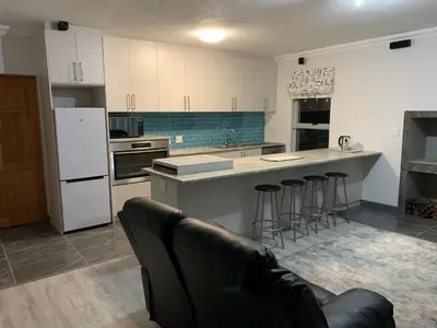 a kitchen with white cabinets and bar stools in it at Bem Vindo Self Catering Guest House in Hermanus