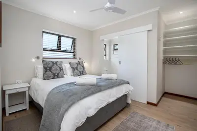 a white bedroom with a bed and a window at Steenbok House in Hermanus