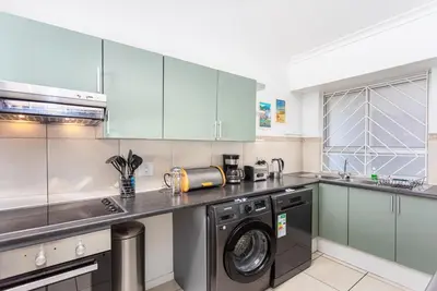 a kitchen with blue cabinets and a washer and dryer at Sea Spray B403 by CTHA in Bloubergstrand