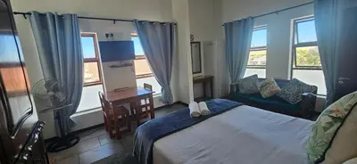 a bedroom with a bed and a desk and windows at Kelkiewyn Guesthouse Caledon in Caledon