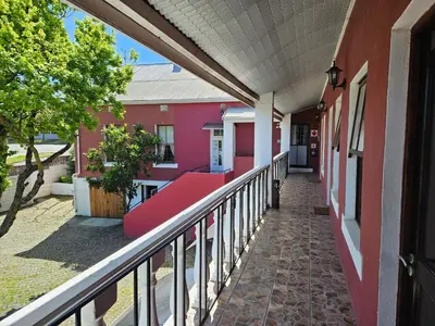 a balcony with a red bench on a pink building at Kelkiewyn Guesthouse Caledon in Caledon