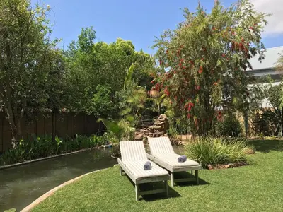 two white chairs sitting on the grass near a pond at B&B Sauvignon Country Lodge in Wellington