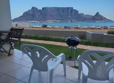 two chairs and a grill on a patio with a view at Sea Spray in Bloubergstrand