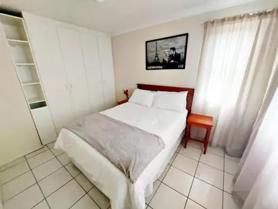 a bedroom with a large white bed and a table at Broadway Self Catering Apartments in Durbanville