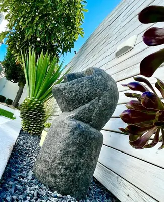 a stone statue sitting on top of rocks in a garden at The Little Palm in Bloubergstrand