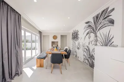 a dining room with a table and chairs with palm wallpaper at The Little Palm in Bloubergstrand