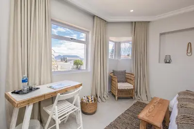 a bedroom with a desk and a bed and a window at The Little Palm in Bloubergstrand