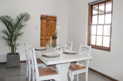 a white dining room table with white chairs and a plant at Langbaai Beach Cottage in Hermanus