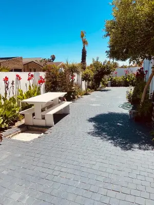 a picnic bench on a brick walkway with flowers at Zagorski’s Bed and breakfast in Bloubergstrand